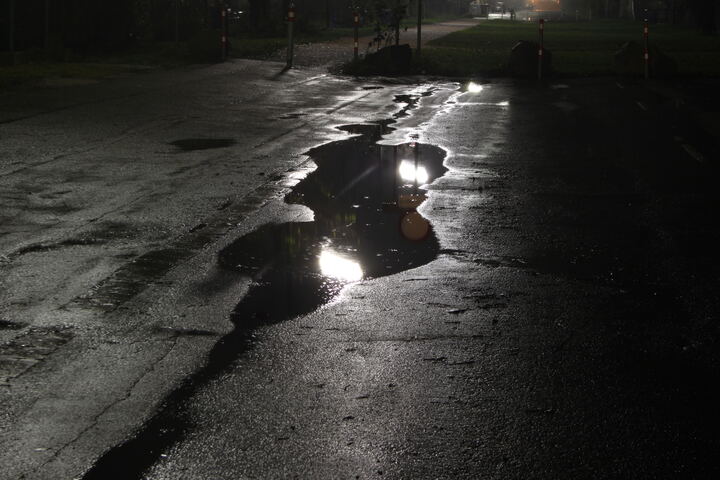 Nasser Asphalt bei Nacht, Lichter spiegeln sich in einer Lacke